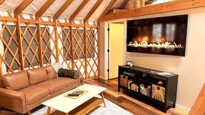 A cozy room with a wooden ceiling, a sofa, a coffee table, a TV, and a fireplace. - Modern Luxury Yurt with Firepit Table & Skylit Dome near Carson, Washington (Carson)