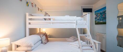 A bunk bed room with white bedding, a nightstand with a lamp, and a painting on the wall.