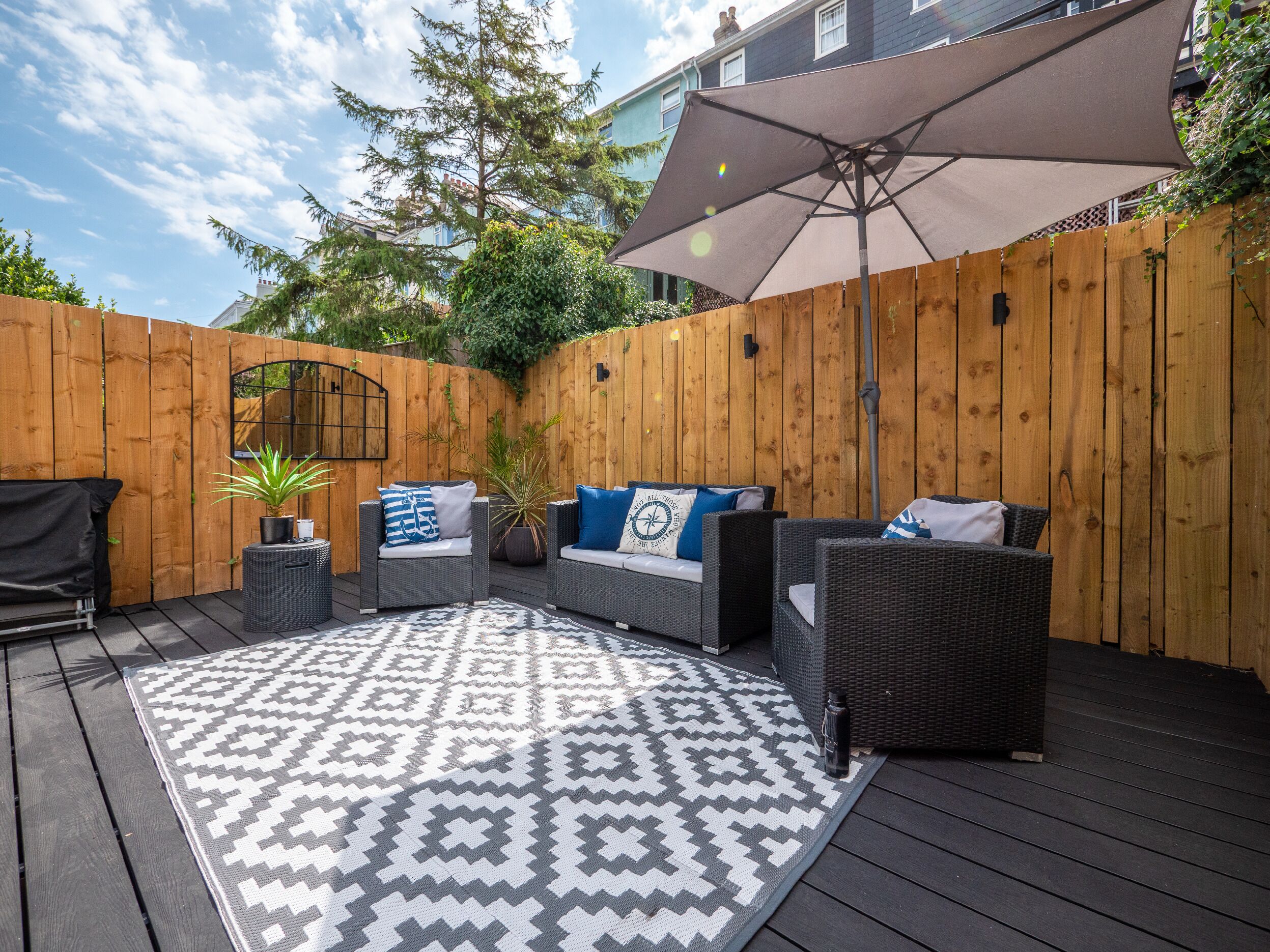 A patio with outdoor furniture, a patterned rug, and a wooden fence.