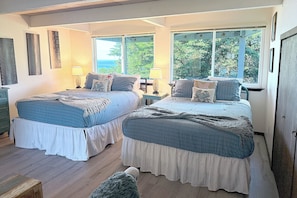 Ein Schlafzimmer mit zwei Betten, Holzboden und großen Fenstern mit Blick auf Grünflächen.