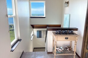 A narrow hallway with a view of the outdoors through a window, a wooden table with glassware, and a small shelf with decorative items. - Dillon Beach~Ocean Views~Hot Tub~Game Room~Dog Friendly~Pacific~Bella Oceana (Dillon Beach)