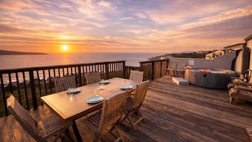 Una terraza de madera con una mesa dispuesta para comer, con vistas al océano al atardecer.
