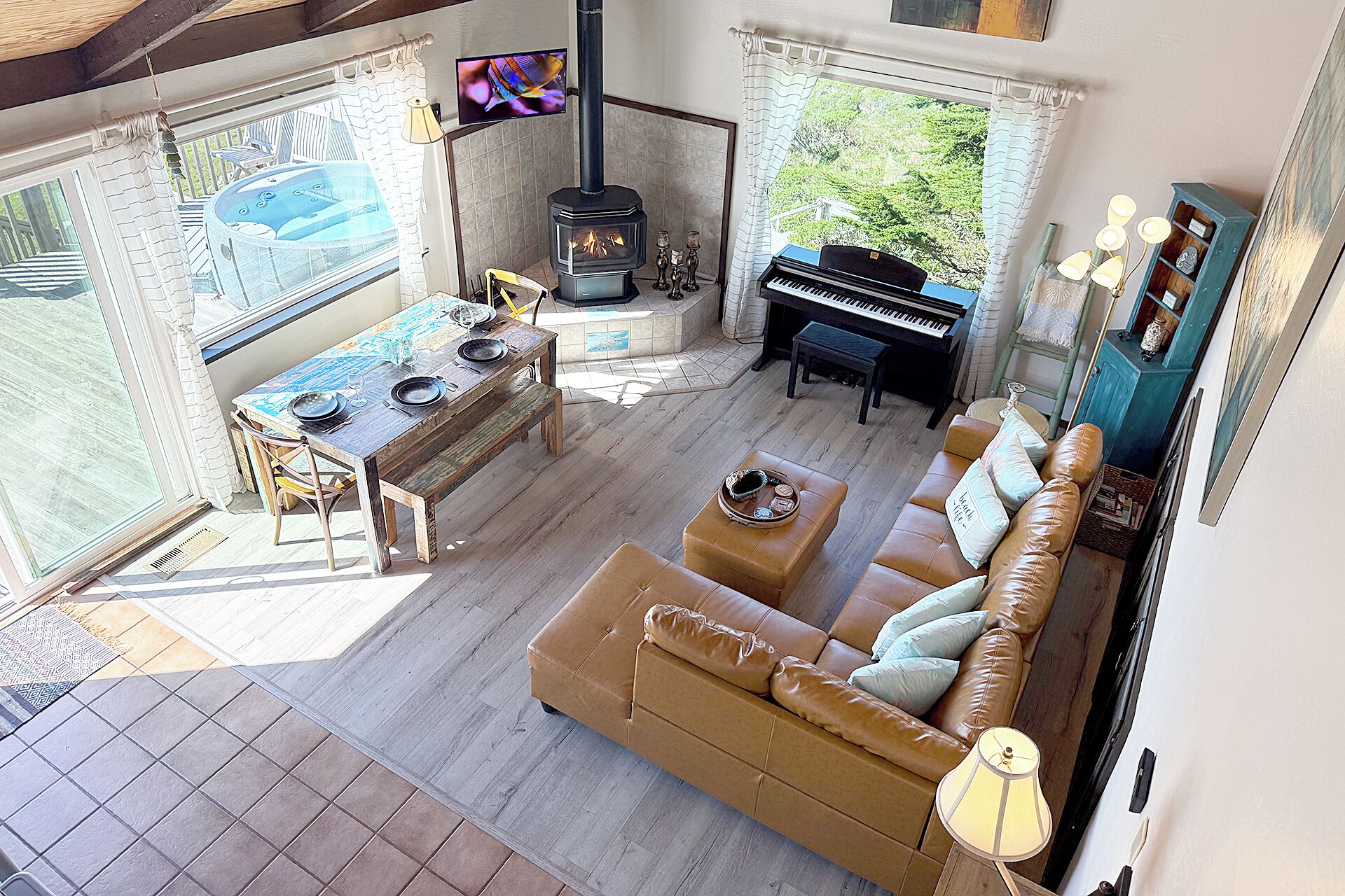 A living room with a sofa, a piano, a table set for dining, a fireplace, and a view of the outdoors.