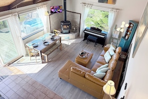 Ein Wohnzimmer mit einer Couch, einem Klavier, einem Esstisch und einem Kamin, mit Blick ins Freie.