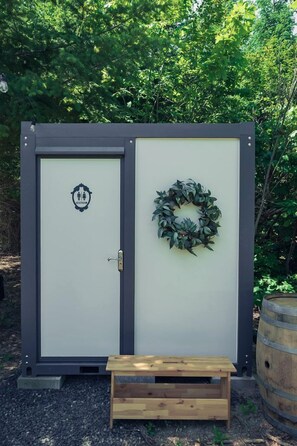 Un lavabo portàtil amb porta, un banc i una corona de flors.