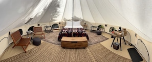 A tent with a bed, chairs, a table, and a rug.