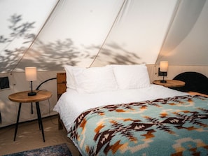A tent with a bed, two bedside tables, and a lamp on each side.