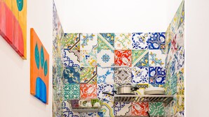 Une cuisine compacte avec des carreaux de couleurs vives, un évier, un petit réfrigérateur et une poubelle.