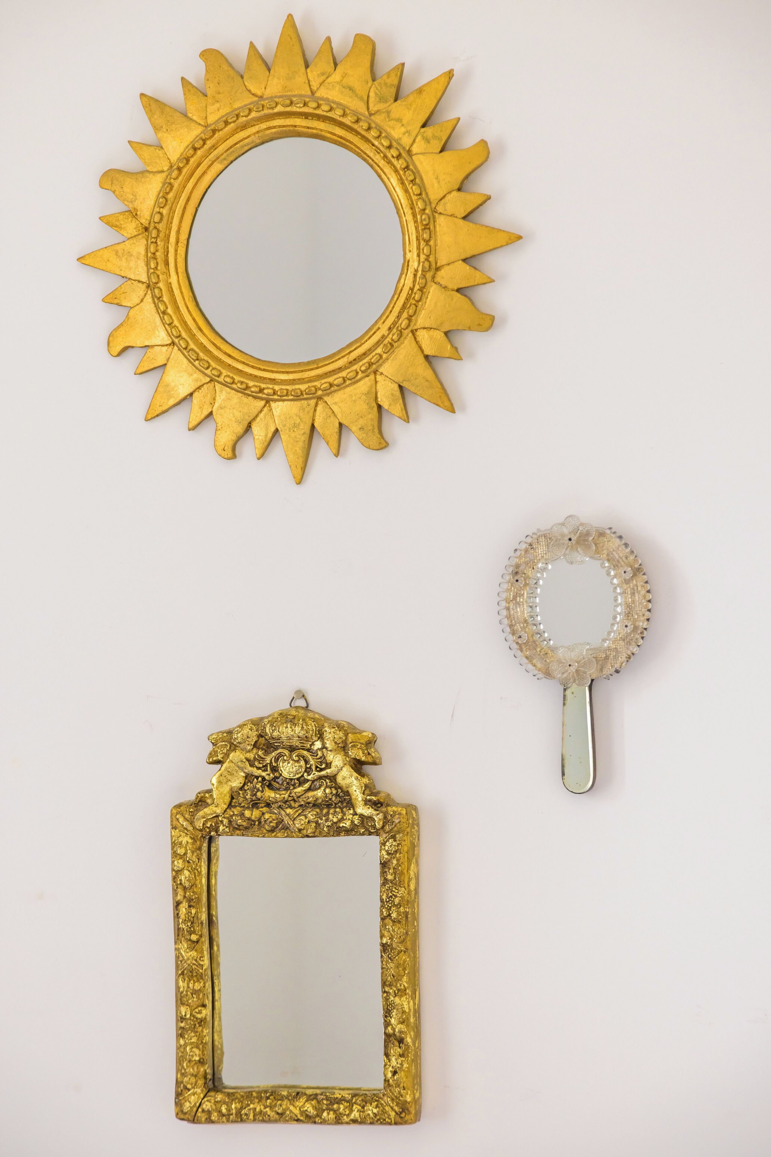 Un miroir décoratif avec un cadre en forme de soleil rayonnant, un petit miroir rond orné de motifs floraux et un miroir rectangulaire avec un cadre travaillé.