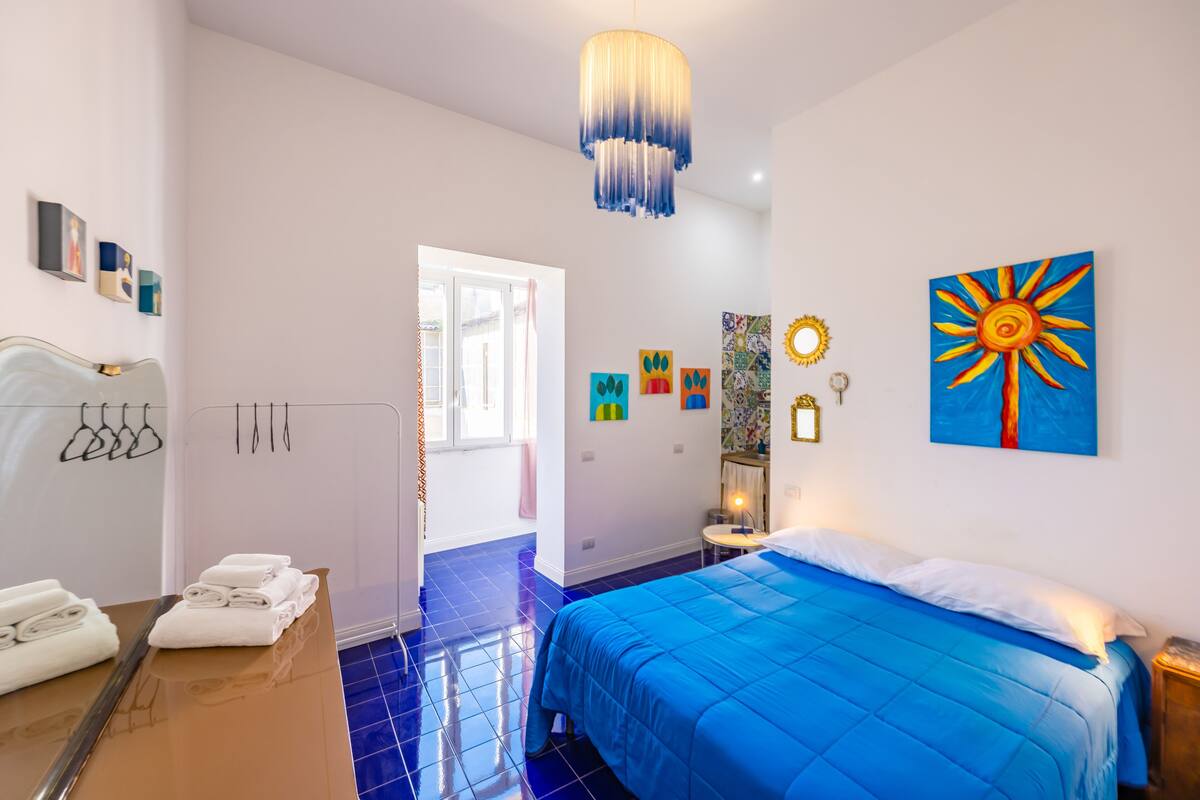 Une chambre d’hôtel avec une couvre-lit bleue, un luminaire suspendu et des œuvres d’art accrochées aux murs.