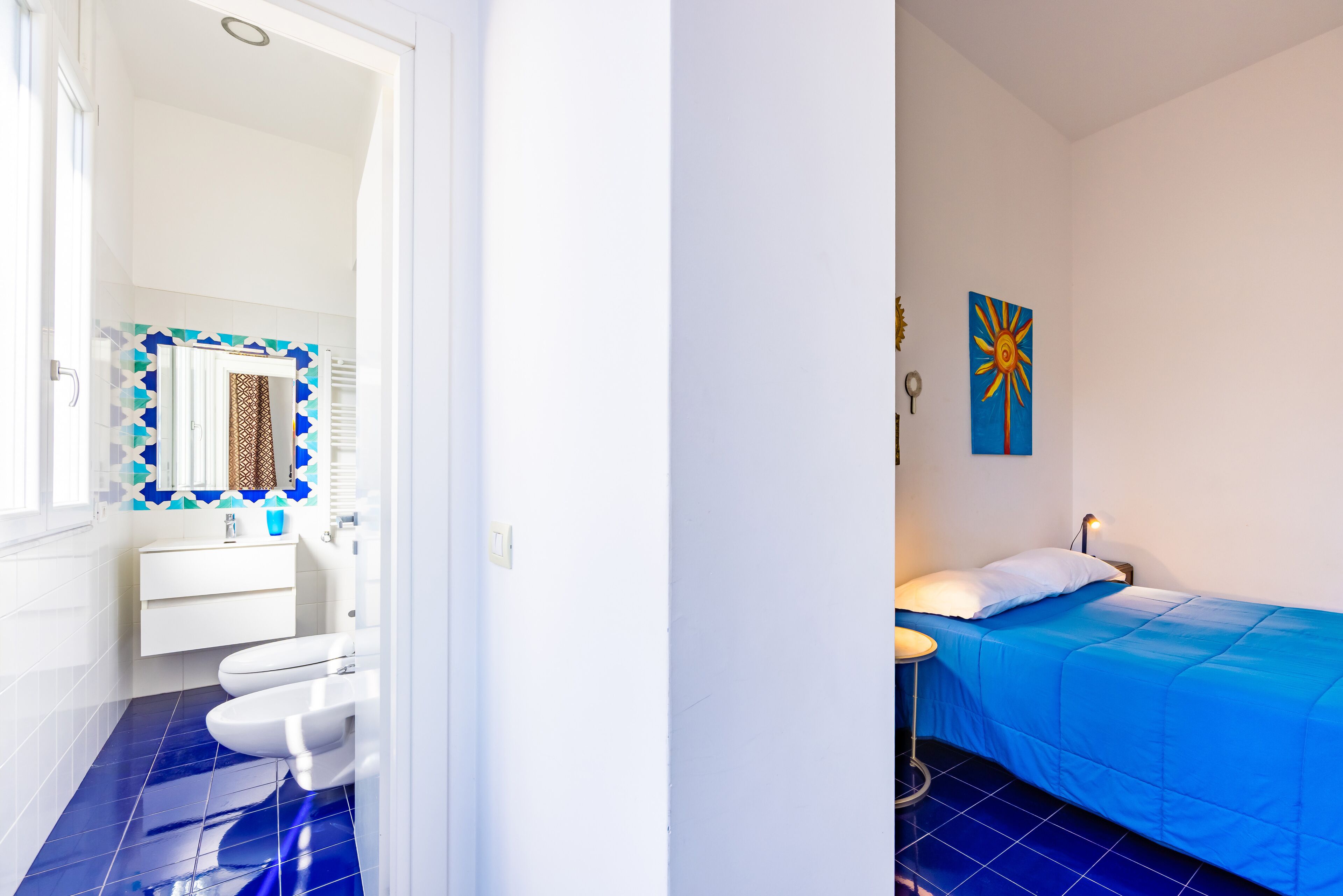 A room with a bed, a bedside table, a window, and a bathroom with a toilet and sink.