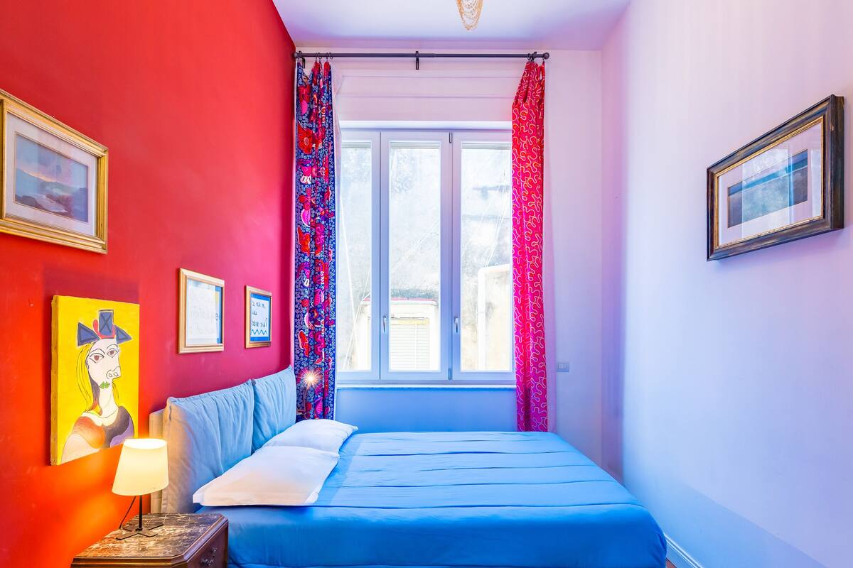 Une chambre à coucher avec un lit, une fenêtre avec des rideaux, un réfrigérateur et un lustre.