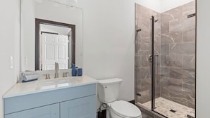 Un baño moderno con un lavamanos blanco, tocador azul y ducha con mampara de vidrio.