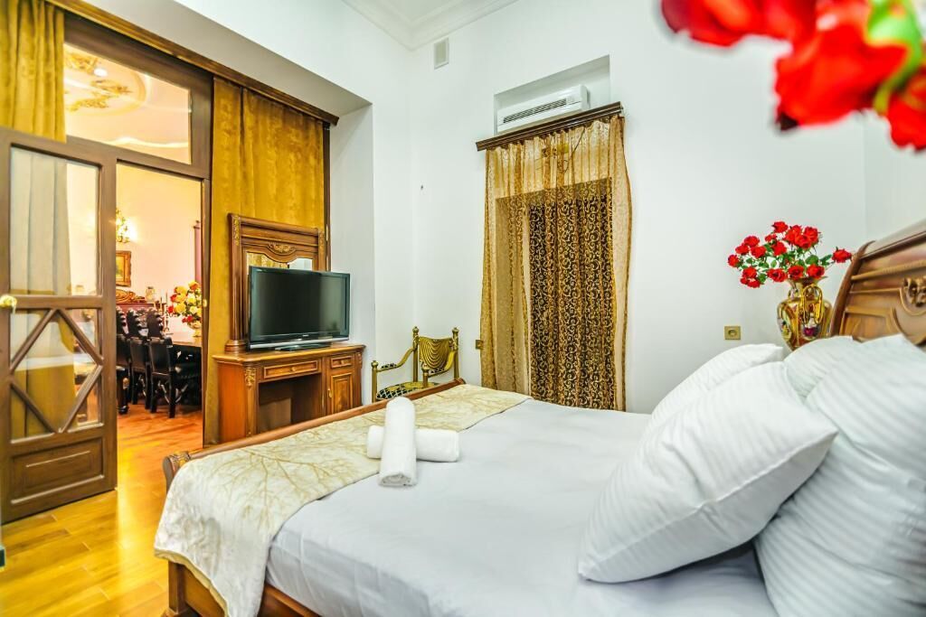 A hotel room with a bed, a television, a wooden dresser, a desk with chairs, and a window with curtains.