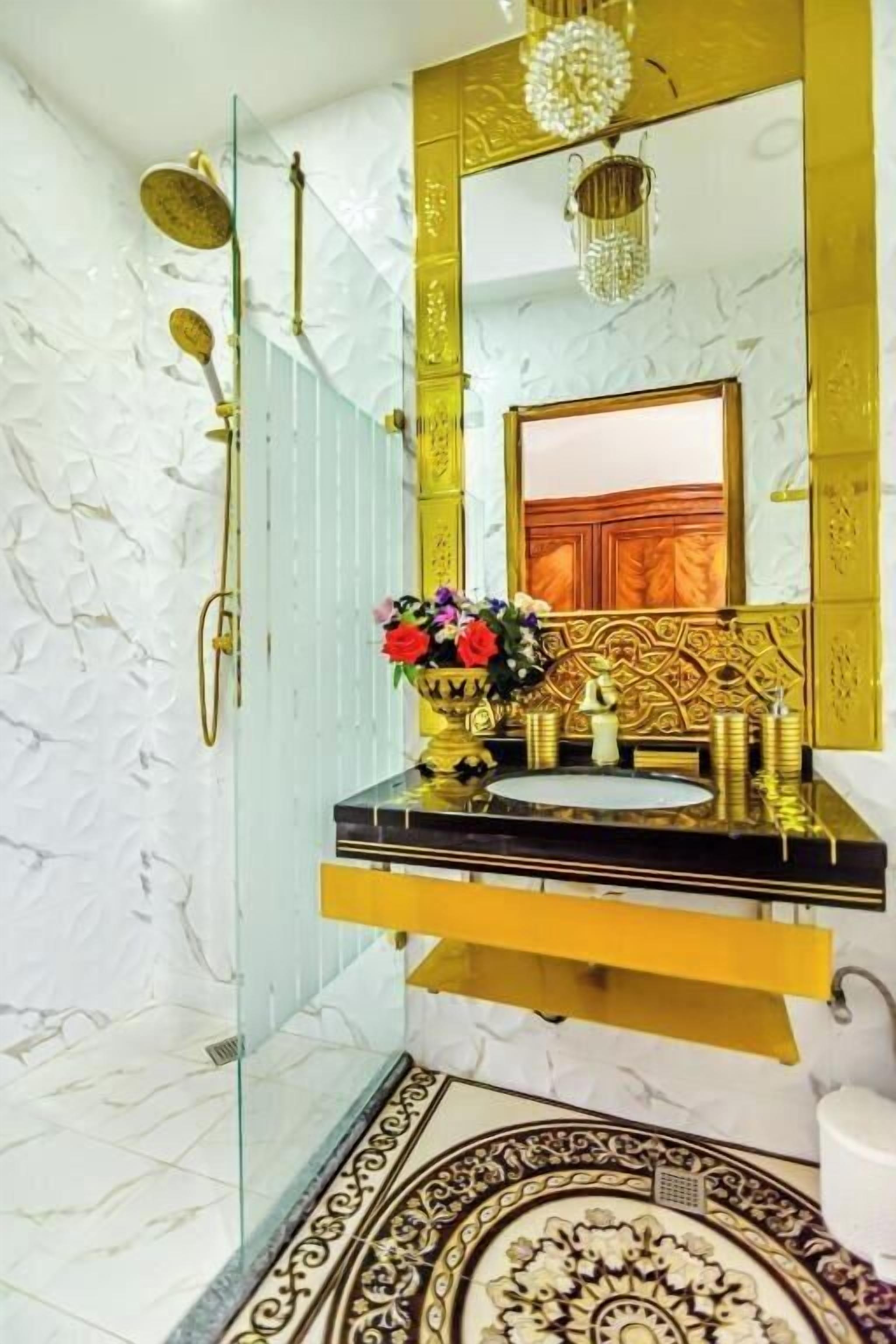 A bathroom with a marble wall, a gold vanity, a large mirror, and a decorative shower area.