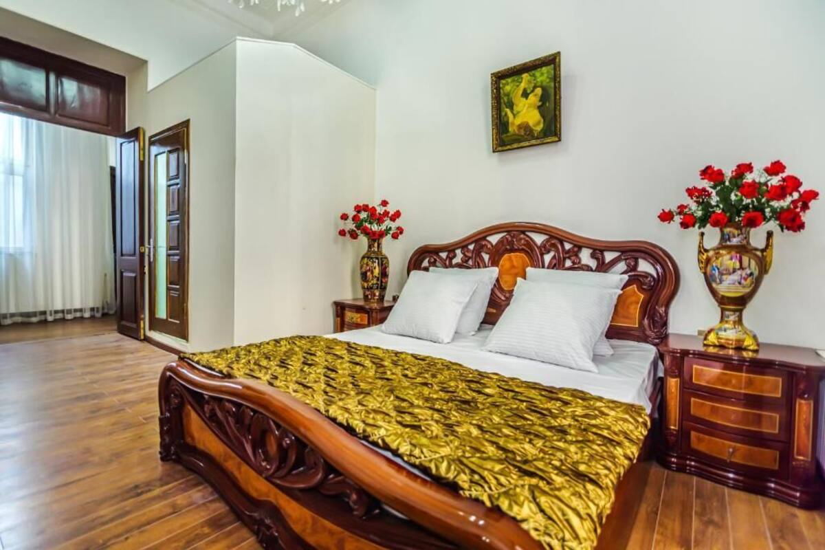 Un dormitorio con cama de madera, ropa de cama blanca, dos mesitas de noche con jarrones de flores y un cuadro en la pared.