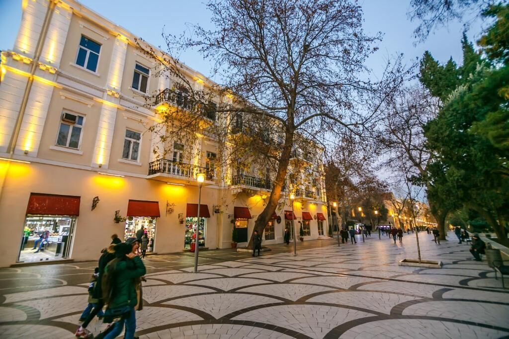 A spacious public square with a tiled floor, surrounded by buildings with balconies and storefronts.