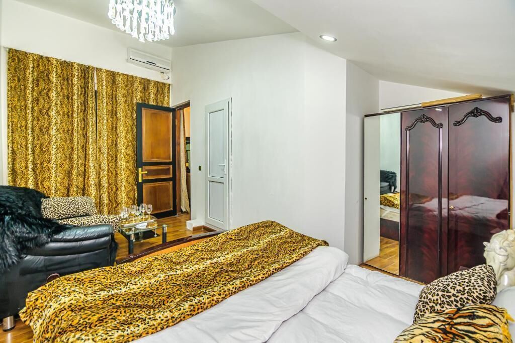 A bedroom with a bed, a wardrobe, a seating area with a chair, and a table with glasses.