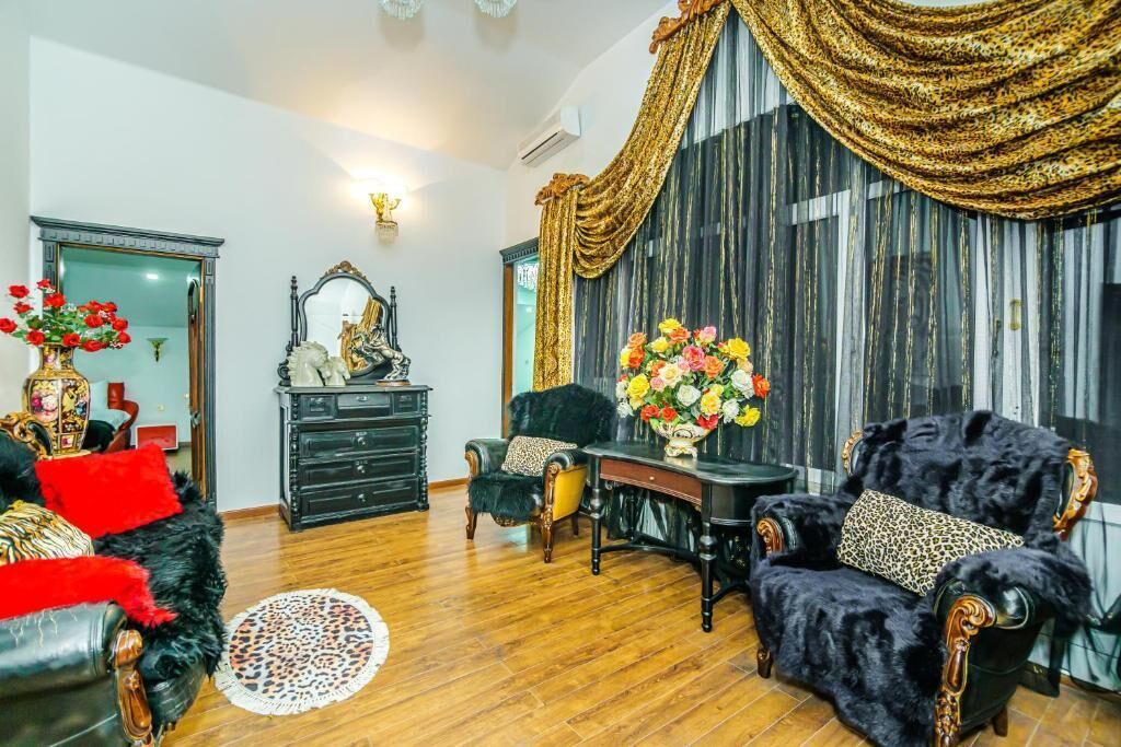 Un salon avec un canapé noir, un fauteuil noir, une table basse en bois et une grande fenêtre ornée de rideaux dorés.