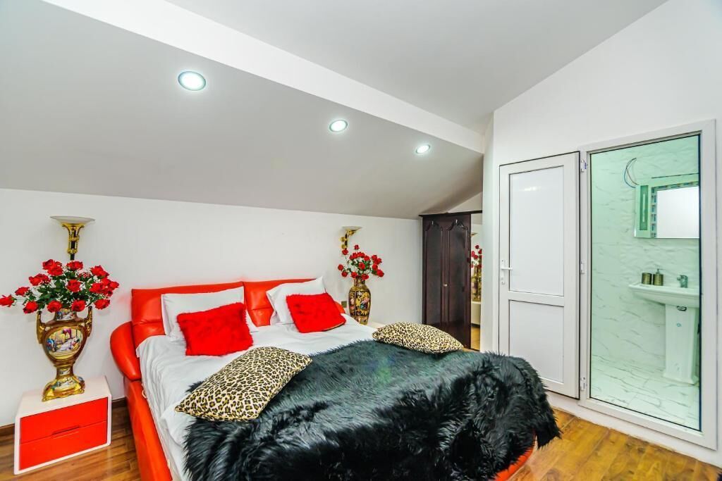 A modern bedroom with a large bed, red and black bedding, and a glass shower enclosure.