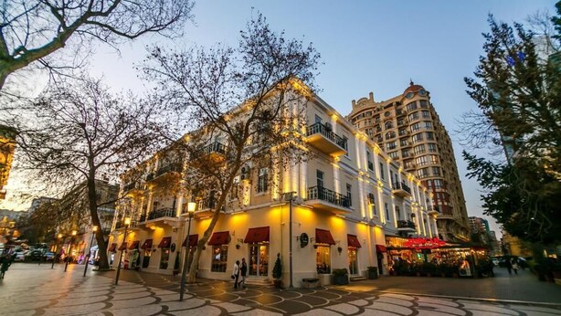 Un hotel de estilo arquitectónico europeo tradicional, con un patio central de pavimento estampado, varios balcones y un toldo rojo.