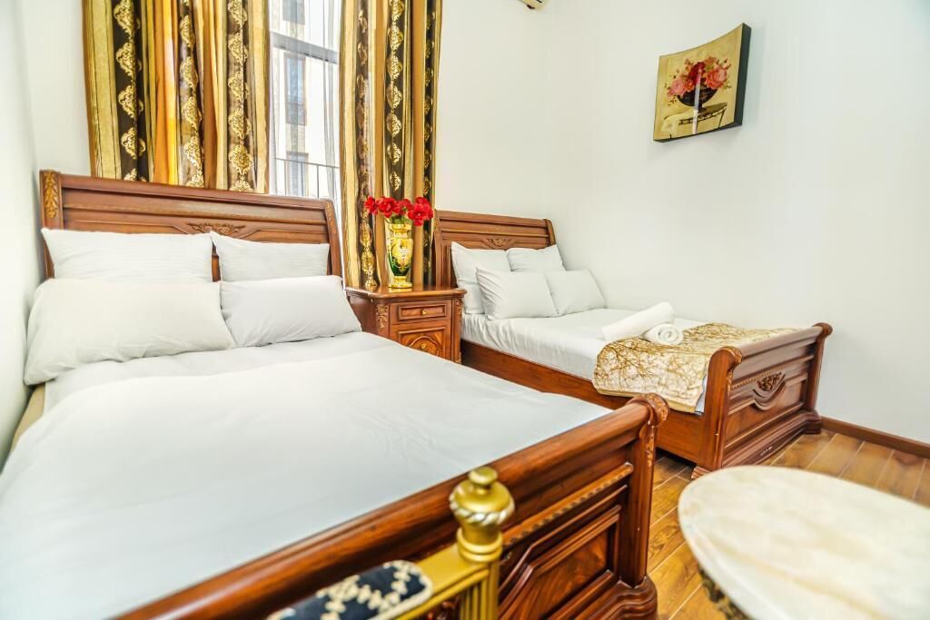 Ein Hotelzimmer mit zwei hölzernen Betten, einem Nachttisch mit einer Vase roter Blumen und einem Gemälde an der Wand.