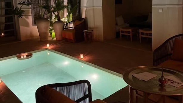 Zona de piscina amb una cadira i taula, envoltada de plantes en testos i una llum càlida.