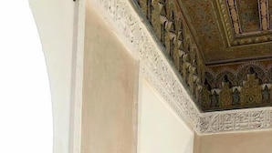 Una habitació amb una paret beix, una cornisa decorativa blanca i una porta amb marc fosc.