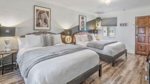 A bedroom with two beds, a nightstand, a lamp, and framed pictures on the wall.