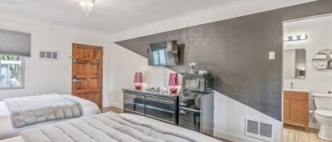 Un dormitorio con dos camas, un aparador, una televisión y un baño visible a través de una puerta abierta.