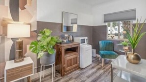 A compact room with a wooden desk, a small refrigerator, a blue chair, and a potted plant. - B. Abstract: Professional Design + King Bed! (Bandon)