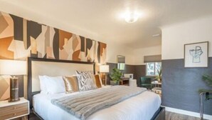A modern hotel room with a large bed, a nightstand, a desk, and a chair. - B. Abstract: Professional Design + King Bed! (Bandon)