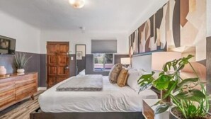 A bedroom with a bed, wooden dresser, and a large abstract painting on the wall. - B. Abstract: Professional Design + King Bed! (Bandon)