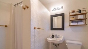 A small bathroom with a shower, a sink, a toilet, and a mirror.