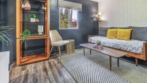 A modern living room with a dark wall, a wooden bookshelf, a sofa with yellow cushions, a coffee table, and a chair.