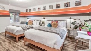 Une chambre d’hôtel avec deux lits, une petite table et une chaise. Il y a des lampes fixées au mur et une fenêtre.