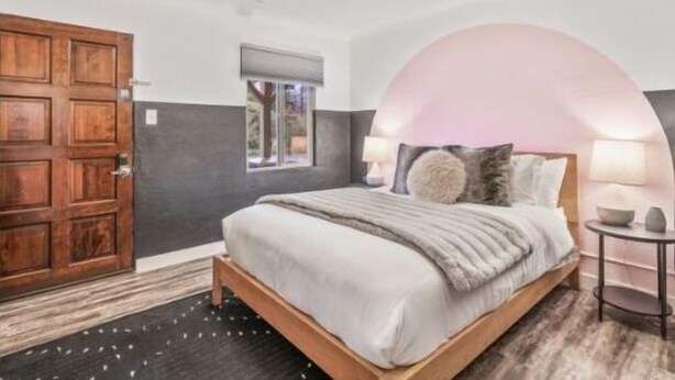 Een slaapkamer met een houten bed, een groot rondboogvenster en een houten deur.