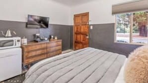 Een slaapkamer met een bed, een houten garderobe, een televisie aan de muur en een raam met uitzicht op bomen.