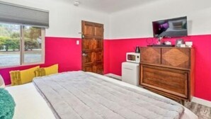 Une chambre à coucher comprenant un lit, une armoire en bois, un téléviseur et une fenêtre donnant sur un paysage verdoyant.