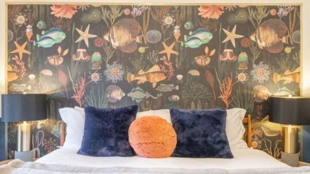 A bed with a floral-patterned headboard, two dark pillows, and a fluffy white bedspread. - b. under the sea #2 King bedroom (Bandon)