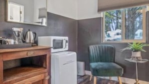 A compact room with a wooden cabinet, a white microwave, a green chair, and a window with a view of trees and a vehicle outside. - b.fresh #6 King bedroom (Bandon)