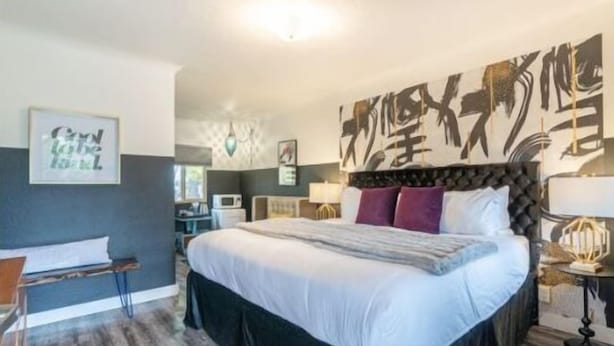 A bedroom with a large bed, a headboard with artwork, a desk, and a chair. - b.fresh #6 King bedroom (Bandon)