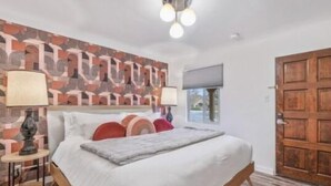 Un dormitorio con una cama, una mesita de noche, una lámpara, una pared con un diseño geométrico y una puerta de madera.