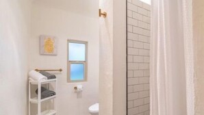 Un baño con inodoro, un estante con toallas, una ventana y una cortina de ducha.
