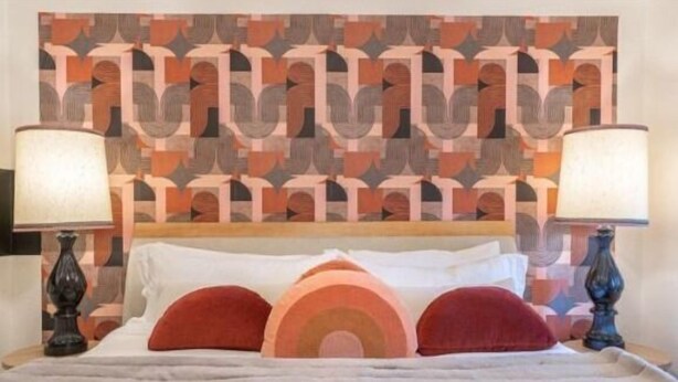 Una cama con cabecera estampada, dos lámparas de noche y tres almohadas.