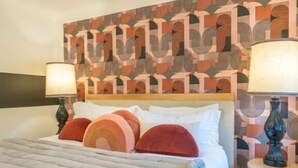 Una habitación de hotel con una cama, dos lámparas de noche y un cabecero estampado.