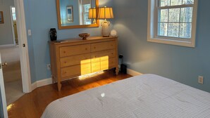 A bedroom with a wooden dresser, a mirror, a lamp, and a window with a view of trees. - Half-Acre Coastal Retreat- Hot tub and walk to town! (Ogunquit)