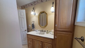 A bathroom with a double sink vanity, wooden cabinets, a mirror, and two wall-mounted lights. - Half-Acre Coastal Retreat- Hot tub and walk to town! (Ogunquit)