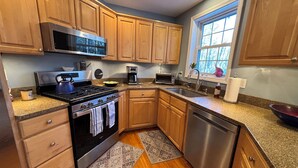 A modern kitchen with wooden cabinets, stainless steel appliances, and a window providing natural light. - Half-Acre Coastal Retreat- Hot tub and walk to town! (Ogunquit)