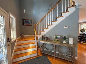 A staircase with wooden steps and white railings, leading to a landing with a console table displaying decorative items. - Half-Acre Coastal Retreat- Hot tub and walk to town! (Ogunquit)